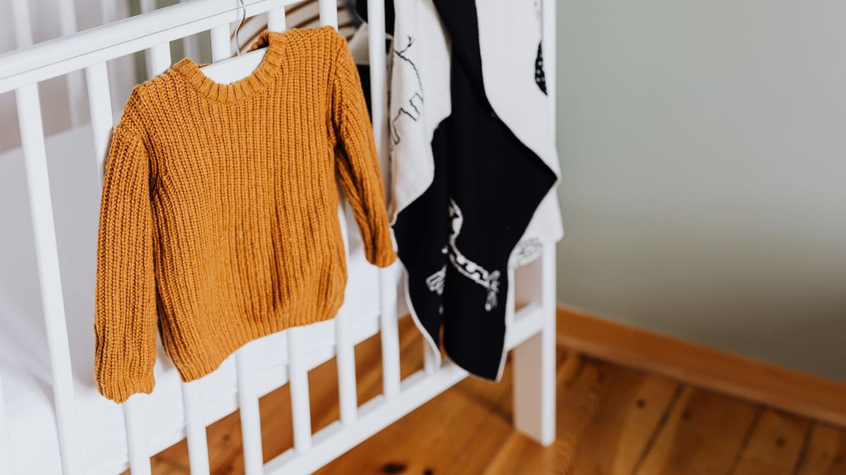 Knitted baby sweater hanging on a white crib in a nursery